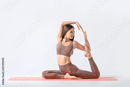 Pretty asian girl sitting in yoga pose on a fitness mat. Excellent flexibility and plasticity of the body.