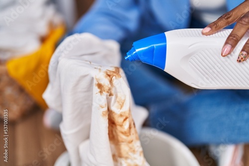 African american woman pouring detergent on dirty t shirt at laundry room