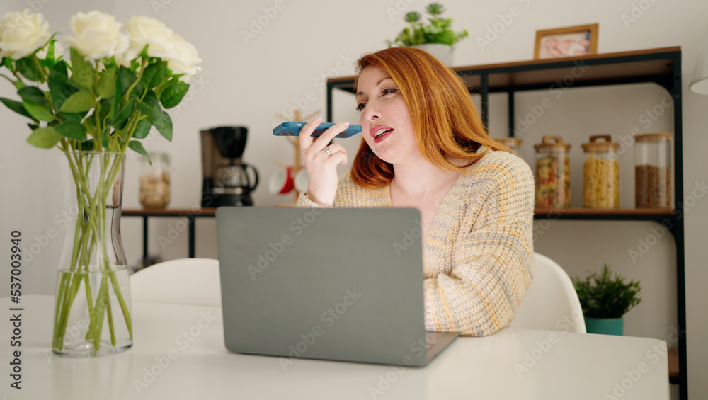 Young redhead woman using laptop and talking on the smartphone at home Young redhead woman using laptop and talking on the smartphone at home