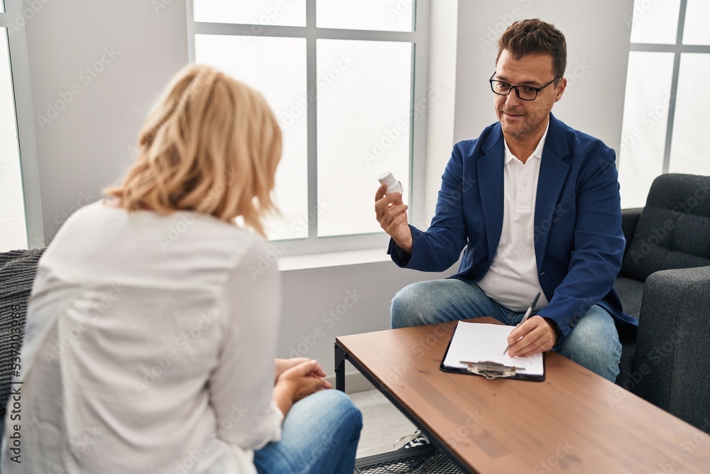 Middle age man and woman pshychologist and patient having pshychology session prescribing pills at psychology center Middle age man and woman pshychologist and patient having pshychology session prescribing pills at psychology center