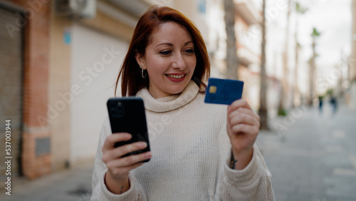 Young redhead woman using smartphone and credit card at street