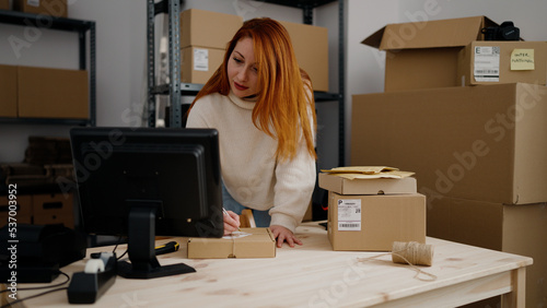 Young redhead woman ecommerce business worker writing on package at office