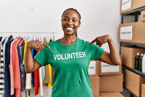 Young african american woman smiling happy pointing with finger to volunteer t shirt at charity center.