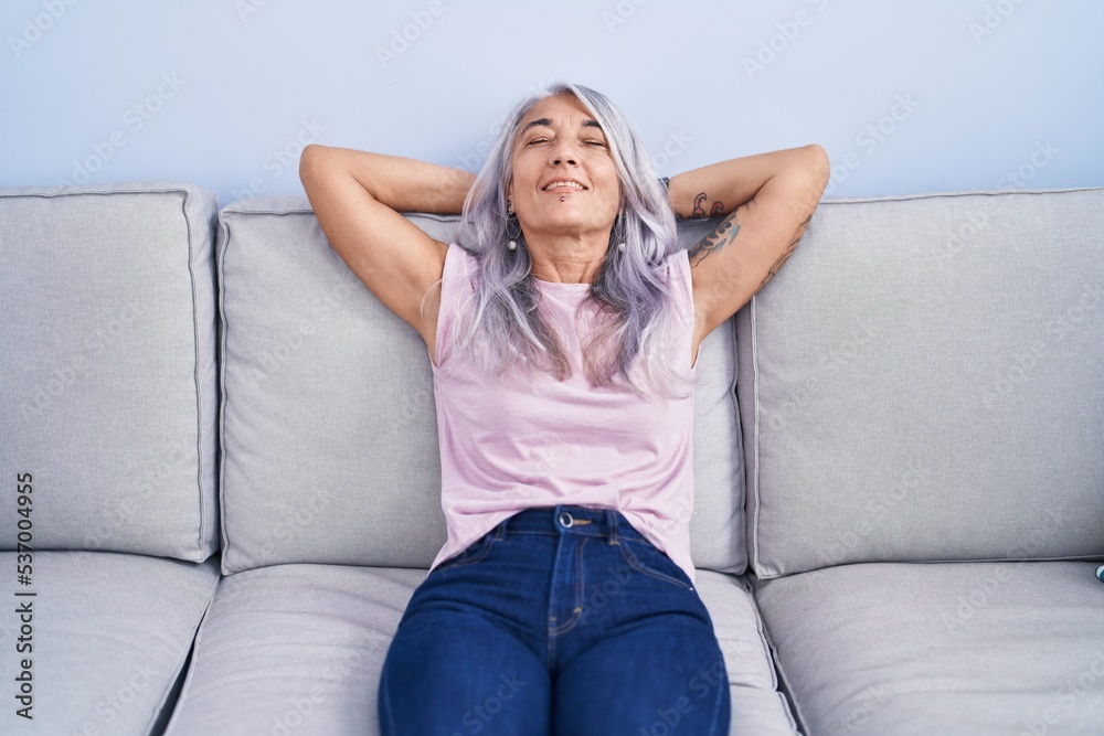 Middle age grey-haired woman relaxed with hands on head sitting on sofa at home Middle age grey-haired woman relaxed with hands on head sitting on sofa at home