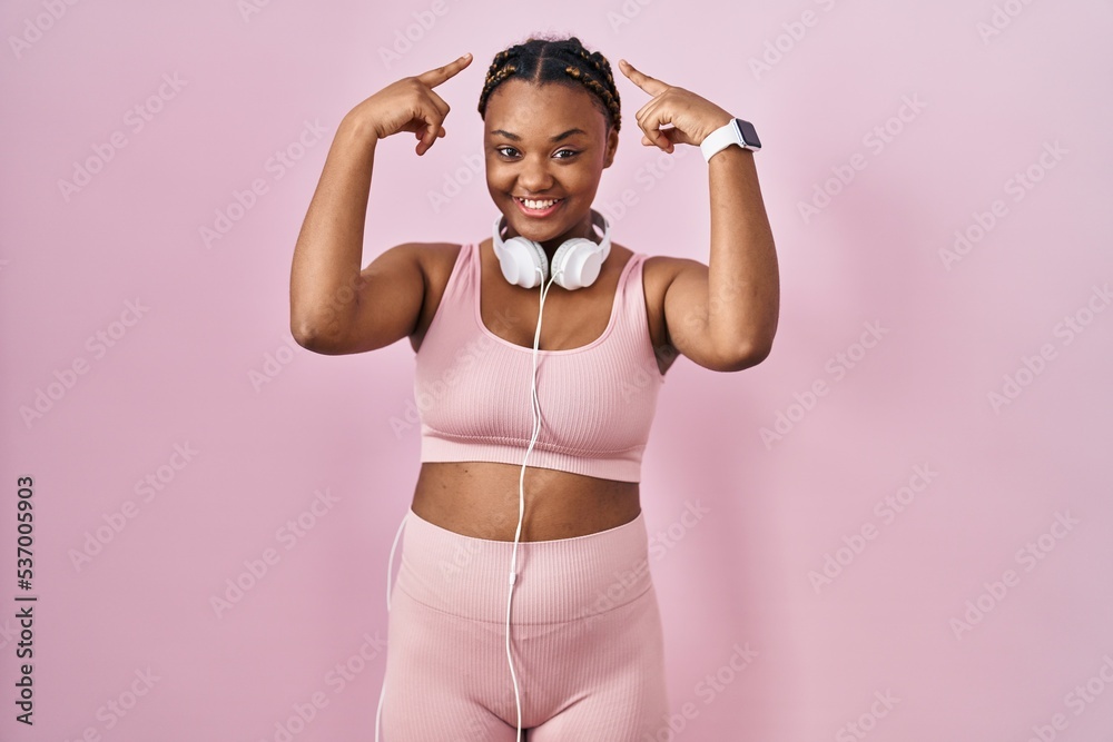 African american woman with braids wearing sportswear and headphones smiling pointing to head with both hands finger, great idea or thought, good memory