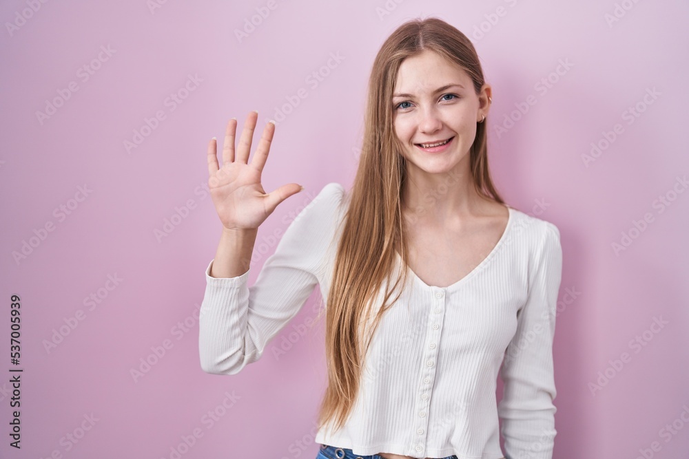 Young caucasian woman standing over pink background showing and pointing up with fingers number five while smiling confident and happy. Young caucasian woman standing over pink background showing and pointing up with fingers number five while smiling confident and happy.