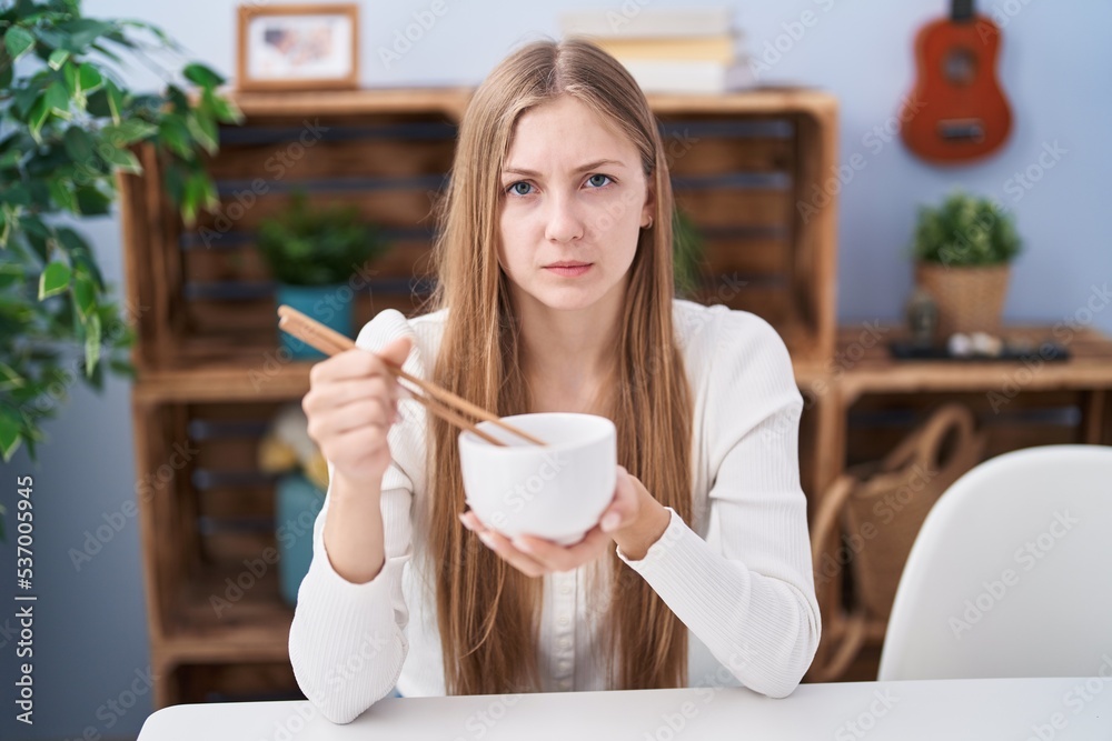 Young caucasian woman eating asian food using chopsticks skeptic and nervous, frowning upset because of problem. negative person. Young caucasian woman eating asian food using chopsticks skeptic and nervous, frowning upset because of problem. negative person.