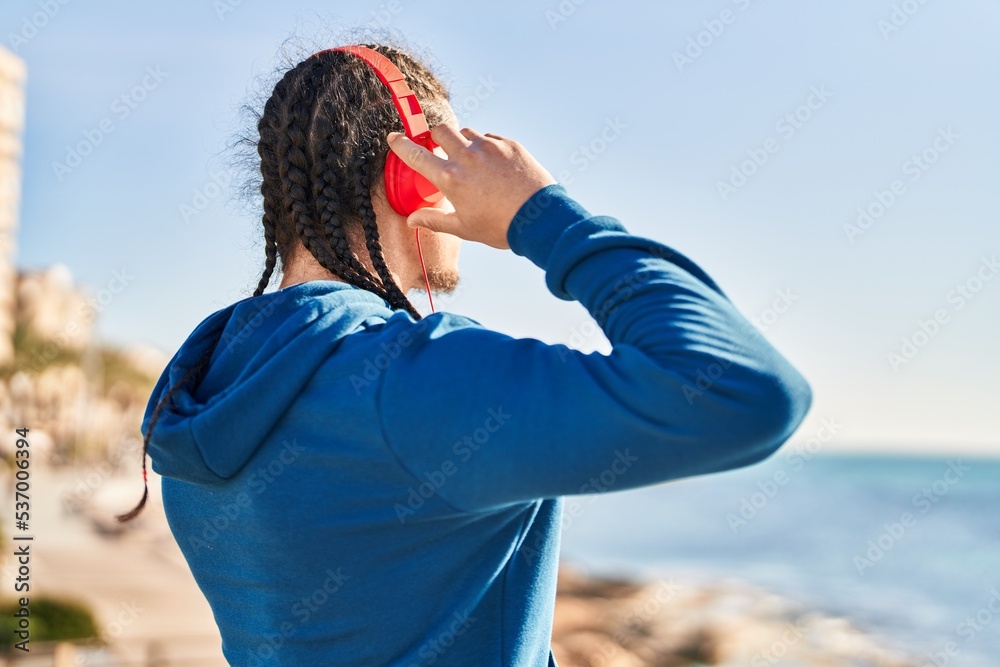 Young man listening to music on back view at seaside