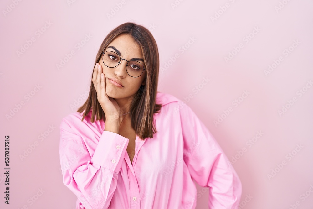 Young hispanic woman wearing glasses standing over pink background thinking looking tired and bored with depression problems with crossed arms.