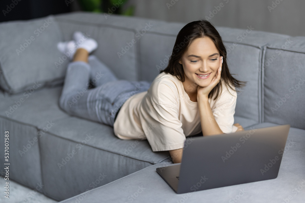 Young Woman using a laptop while relaxing on the couch Young Woman using a laptop while relaxing on the couch