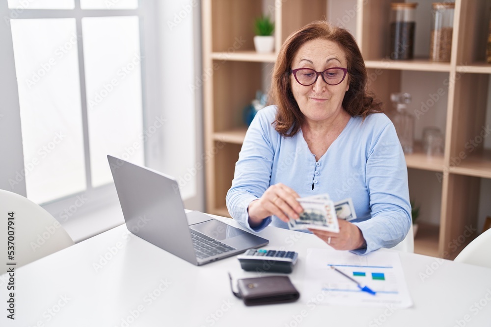 Senior woman using laptop counting dollars at home Senior woman using laptop counting dollars at home