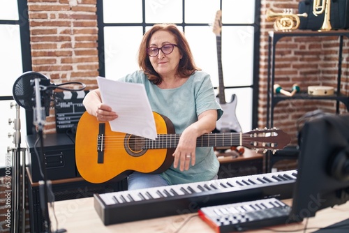Senior woman musician playing classical guitar reading paper at music studio