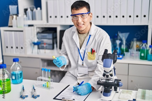 Young man scientist writing on document measuring liquid at laboratory