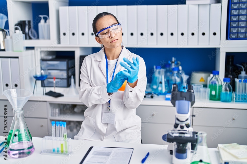 Young hispanic woman scientist wearing gloves at laboratory