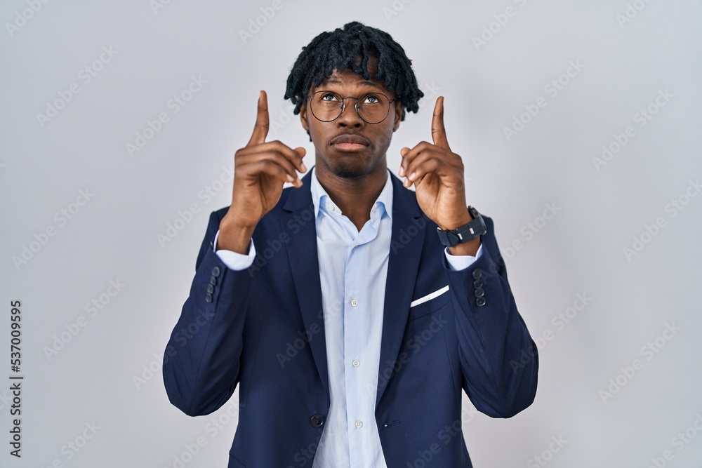 Young african man with dreadlocks wearing business jacket over white background pointing up looking sad and upset, indicating direction with fingers, unhappy and depressed. Young african man with dreadlocks wearing business jacket over white background pointing up looking sad and upset, indicating direction with fingers, unhappy and depressed.