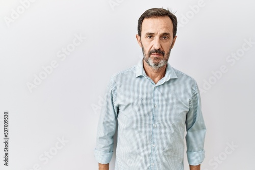 Middle age hispanic man with beard standing over isolated background relaxed with serious expression on face. simple and natural looking at the camera.