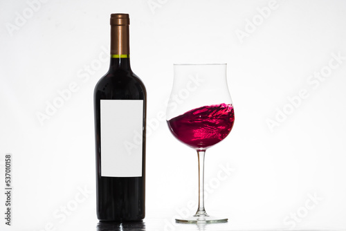 bottle of wine, with tulip glass with red wine in motion, winery, white background.