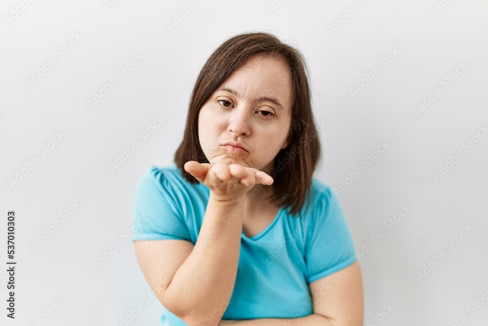 Young down syndrome woman standing over isolated background looking at the camera blowing a kiss with hand on air being lovely and sexy. love expression. Young down syndrome woman standing over isolated background looking at the camera blowing a kiss with hand on air being lovely and sexy. love expression.