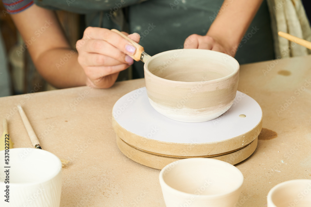 Close-up of girl painting clay mug with glaze. Woman coloring pottery in workshop with a paintbrush. Painter in green apron glazing clay pot. Close-up of girl painting clay mug with glaze. Woman coloring pottery in workshop with a paintbrush. Painter in green apron glazing clay pot.