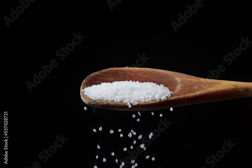 Large rock sea salt on a black background. Salt pouring from a wooden spoon