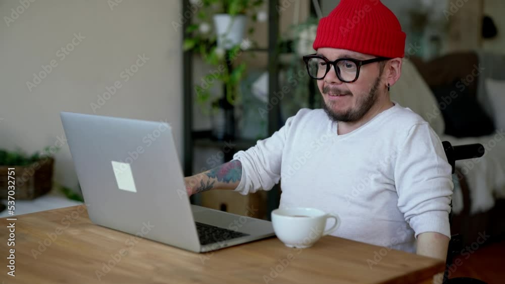 Young man with disability wearing red cap talking in video conference Young man with disability wearing red cap talking in video conference