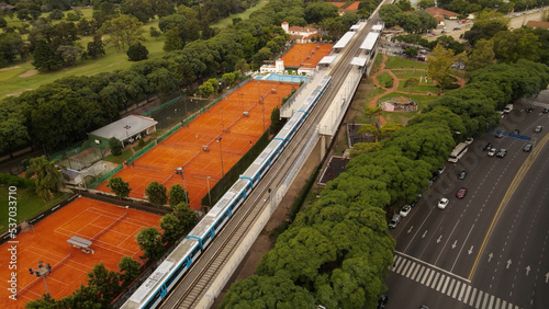 Train passing on railroad between Libertador Avenue and tennis court at Barrancas de Belgrano, Buenos Aires. Aerial drone view photo