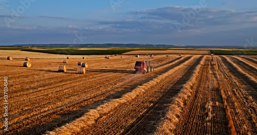 Agricultural farm tractor baler in action on a harvested wheat field