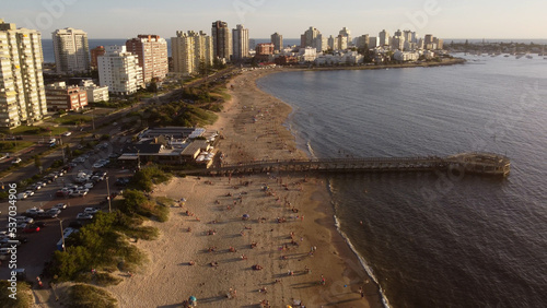 Long pier on crowded beach of Punta del Este in Uruguay at sunset . Aerial panoramic view