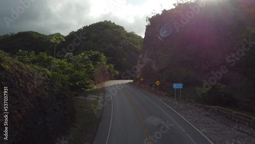 Aerial drone video of a road in the middle of a tropical mountain forest with sun rays in the Dominican Republic. 