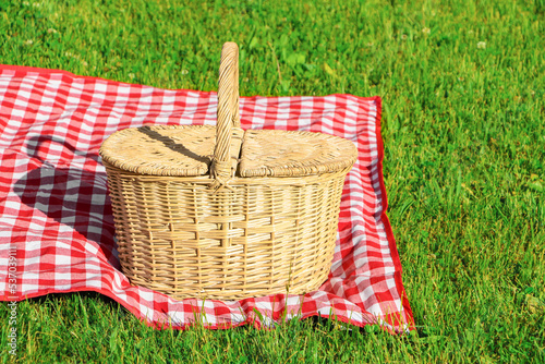 Fototapeta Naklejka Na Ścianę i Meble -  Picnic basket with checkered tablecloth on green grass outdoors