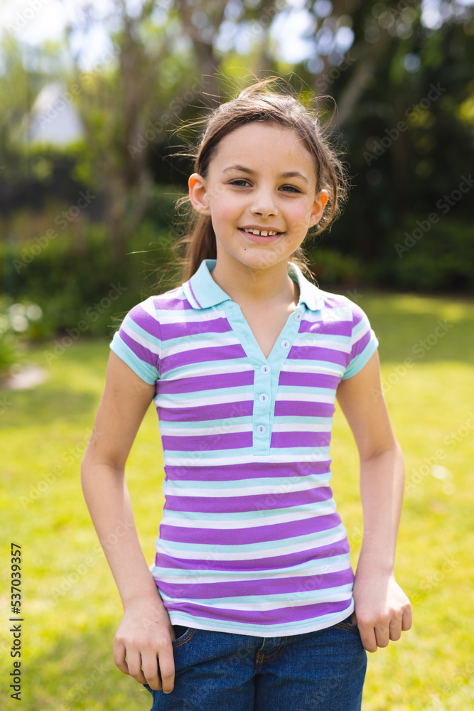 Vertical portrait of young caucasian girl wearing striped t-shirt and standing in the garden Vertical portrait of young caucasian girl wearing striped t-shirt and standing in the garden