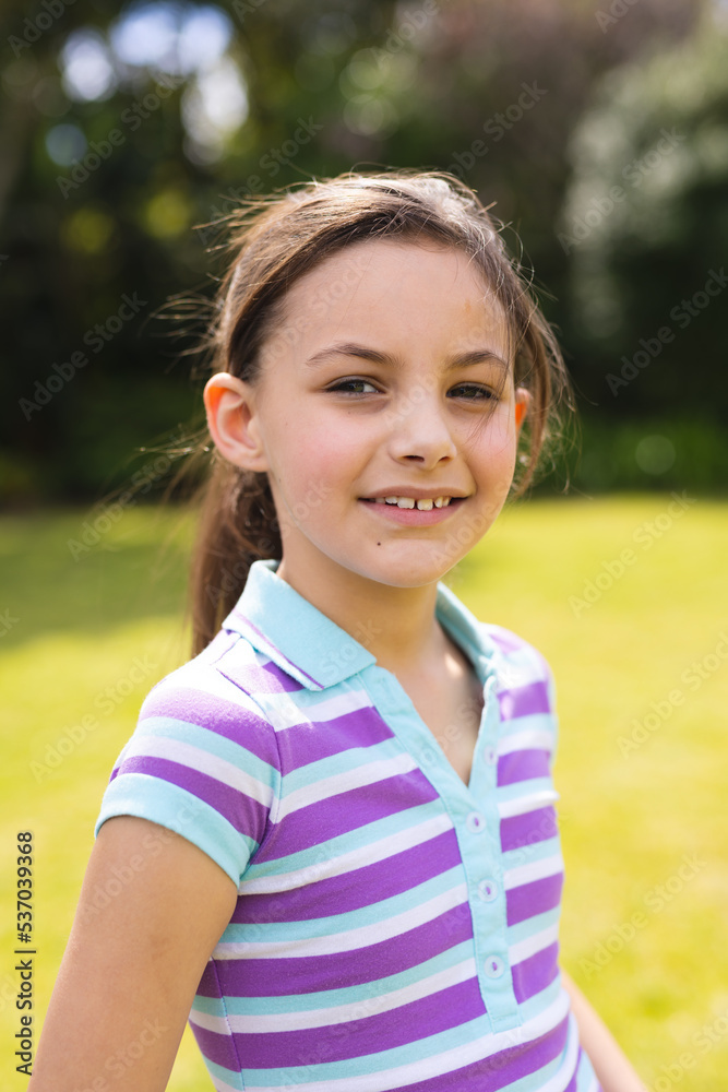 Vertical portrait of young caucasian girl wearing striped t-shirt and standing in the garden Vertical portrait of young caucasian girl wearing striped t-shirt and standing in the garden