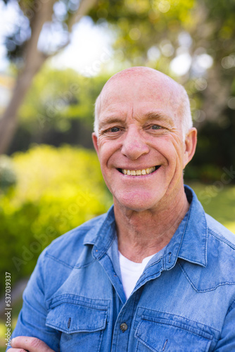 Vertical portrait of senior caucasian men wearing blue shirt and standing in the garden