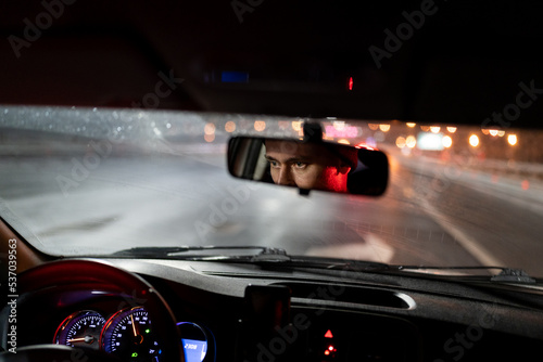 Konstfotografi Look of man is reflected in rear-view mirror traveling in car in evening hurries home after work