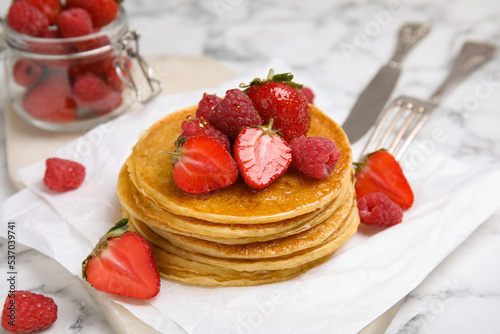 Tasty pancakes with fresh berries and honey on white marble table