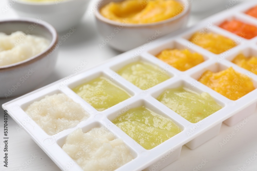 Different purees in ice cube tray and bowls on white table, closeup. Ready for freezing Different purees in ice cube tray and bowls on white table, closeup. Ready for freezing