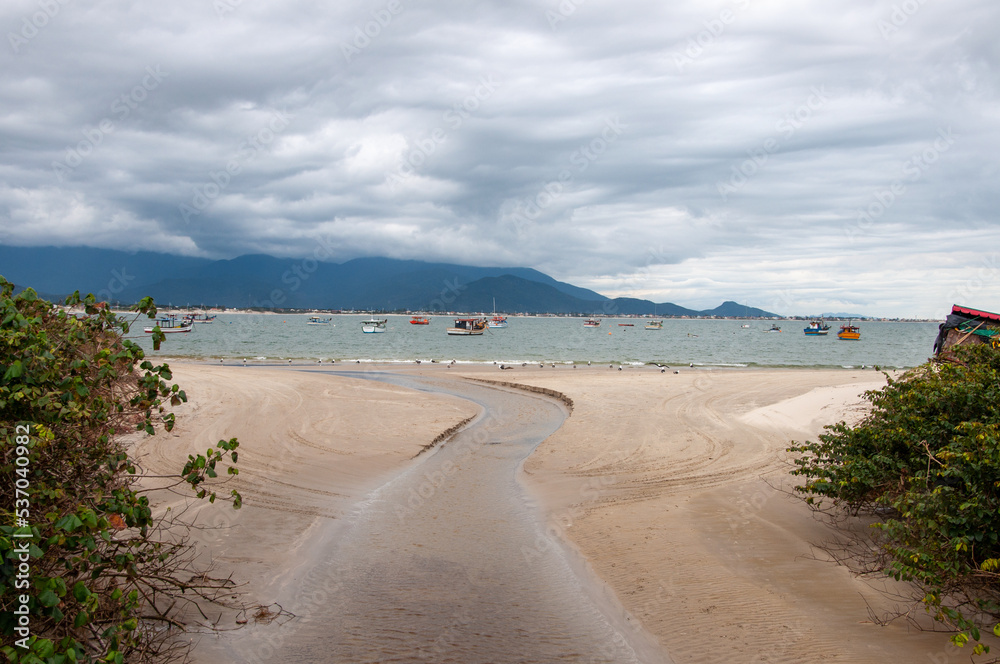 Small stream flowing into the sea with boats and mountains in the background