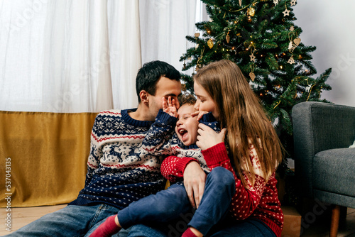 Happy family sitting on floor near Christmas tree.