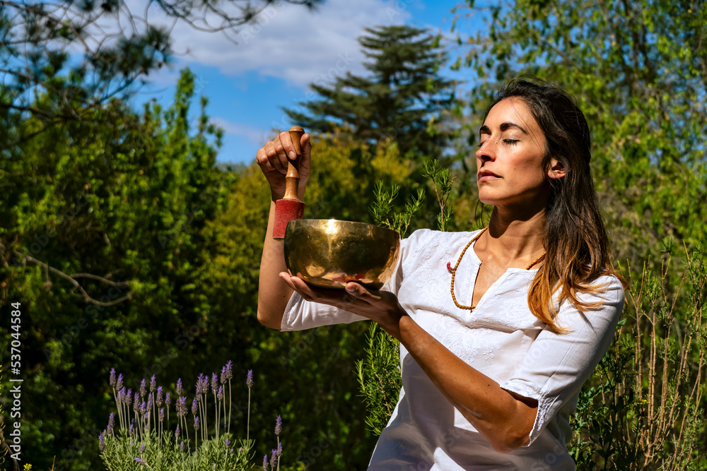 Young woman feeling the vibration of a Tibetan singing bowl outdoors. Young woman feeling the vibration of a Tibetan singing bowl outdoors.