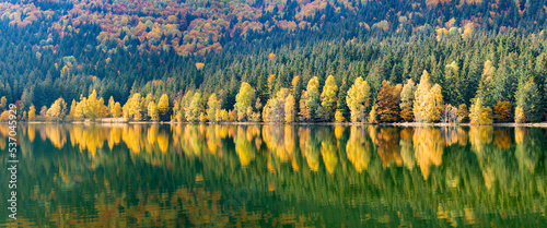 Landscape with yellowed trees mirrored in the water of Saint Ana lake
