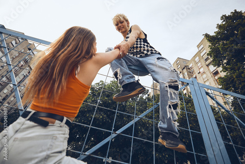 Fotografie A teenage boy is helping his girlfriend climb up the railing in the urban exterior