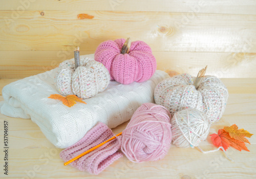 beige and soft pink crochet woolen pumpkin obn a white woolen blanket with woolen balls, crocjet hook and autumn leaves on wooden ground