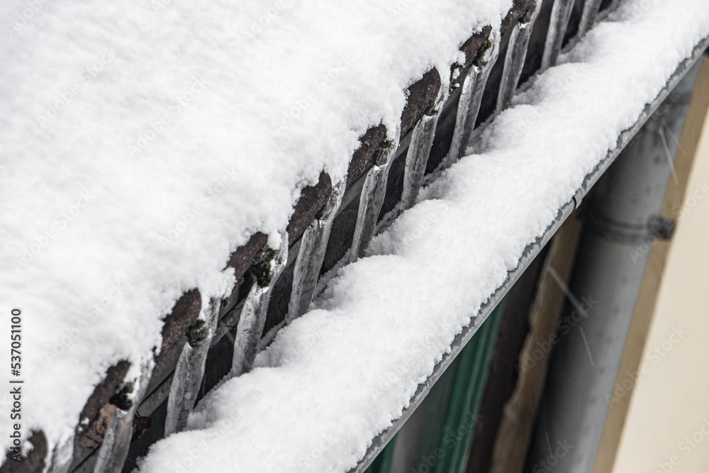 Obraz premium The water freeze on the roof when flows to the spout. Frozen outflow of water from the roof of the house. Icicles on a snowy roof.