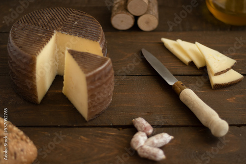 Manchego cheese board on wooden board with nuts on a dark rustic background.