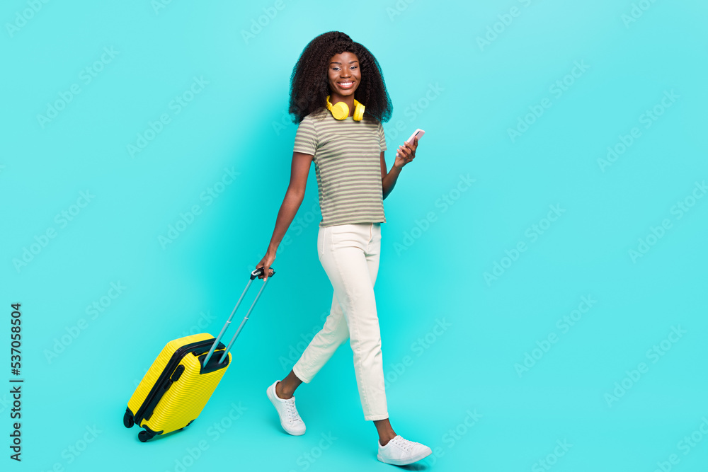Full body profile photo of attractive lady hold telephone suitcase walking isolated on teal color background Full body profile photo of attractive lady hold telephone suitcase walking isolated on teal color background