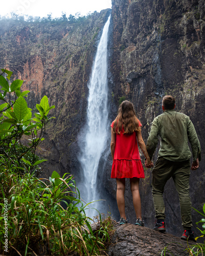 pair of hikers stand beneath australia's largest waterfall, wallaman falls, queensland; vacation in queensland, hiking to mighty waterfall