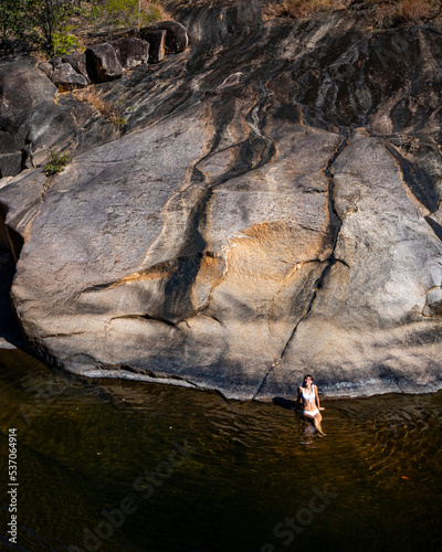 a beautiful girl in a white bikini lies on the water in a natural pool surrounded by massive rocks in jourama falls; relaxing in paluma range national park in queensland, australia; cascading waterfal