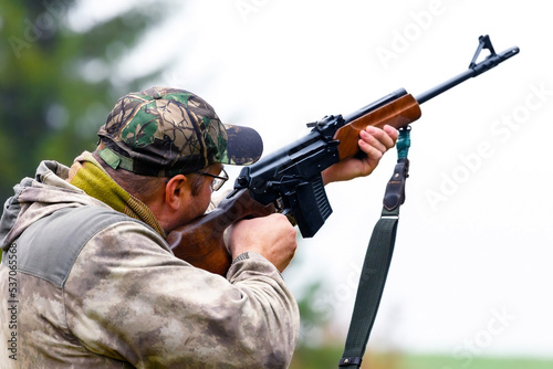 A man takes aim and shoots a combat carbine or guns in blurry focus at targets in a shooting range. Back view of a shooting hunter during hunting.
