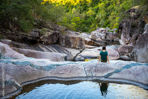 girl with pigtails sits on colorful rocks at jourama falls at sunset; relaxing at paluma range national park in queensland, australia; cascading waterfalls with pools photo