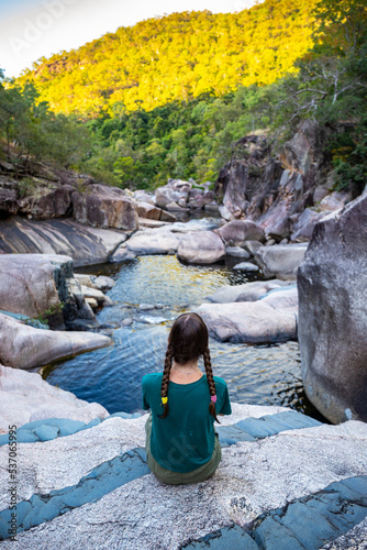 girl with pigtails sits on colorful rocks at jourama falls at sunset; relaxing at paluma range national park in queensland, australia; cascading waterfalls with pools photo